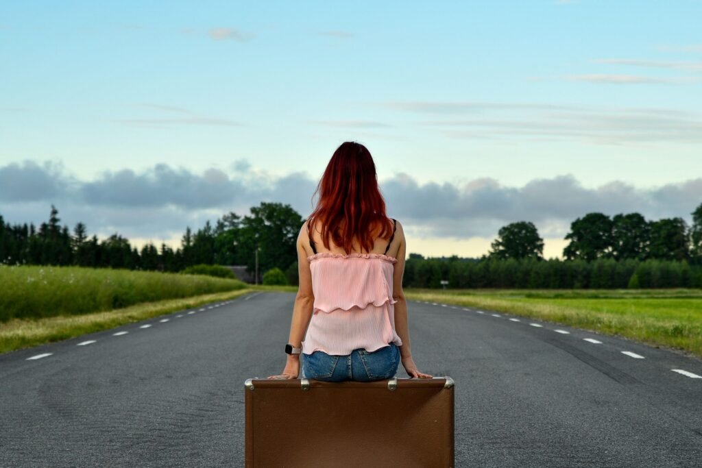 Donna seduta su una valigia lungo una strada di campagna durante un viaggio lento.
