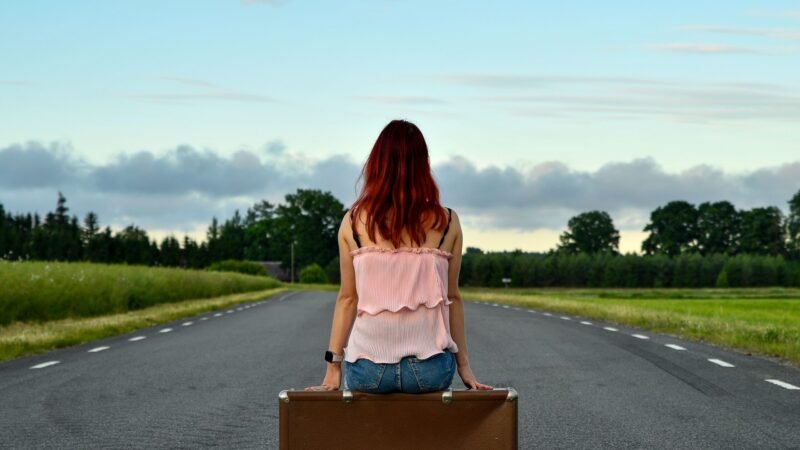 Donna seduta su una valigia lungo una strada di campagna durante un viaggio lento.